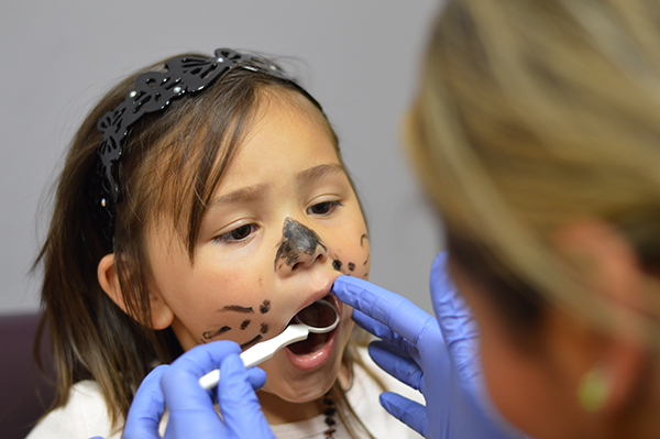 Little girl with her face painted like a kitty cat gets her teeth checked by a dentist.