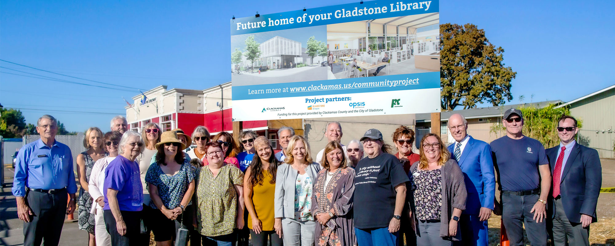 Elected officials and community members standing in front of the new sign in front of the location of the future Gladstone Library