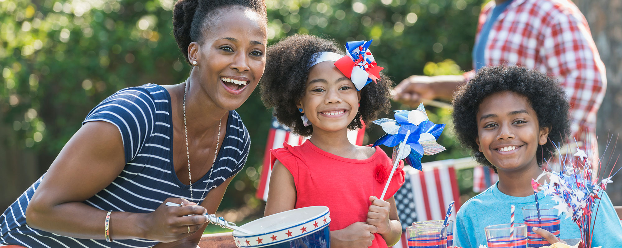 A family sitting together at a picnic table for a Fourth of July barbecue in their backyard