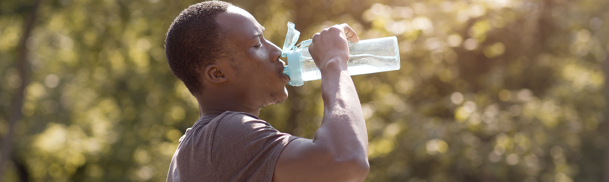 Man drinking water from a water bottle while outside on a hot day