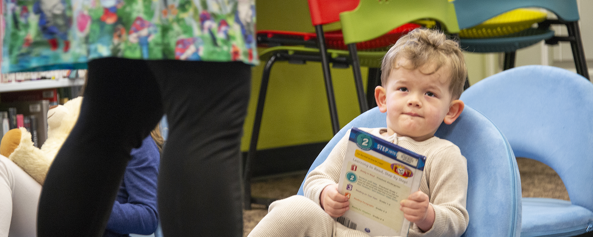 Small boy in blue chair listens intently to storytime while he holds a book