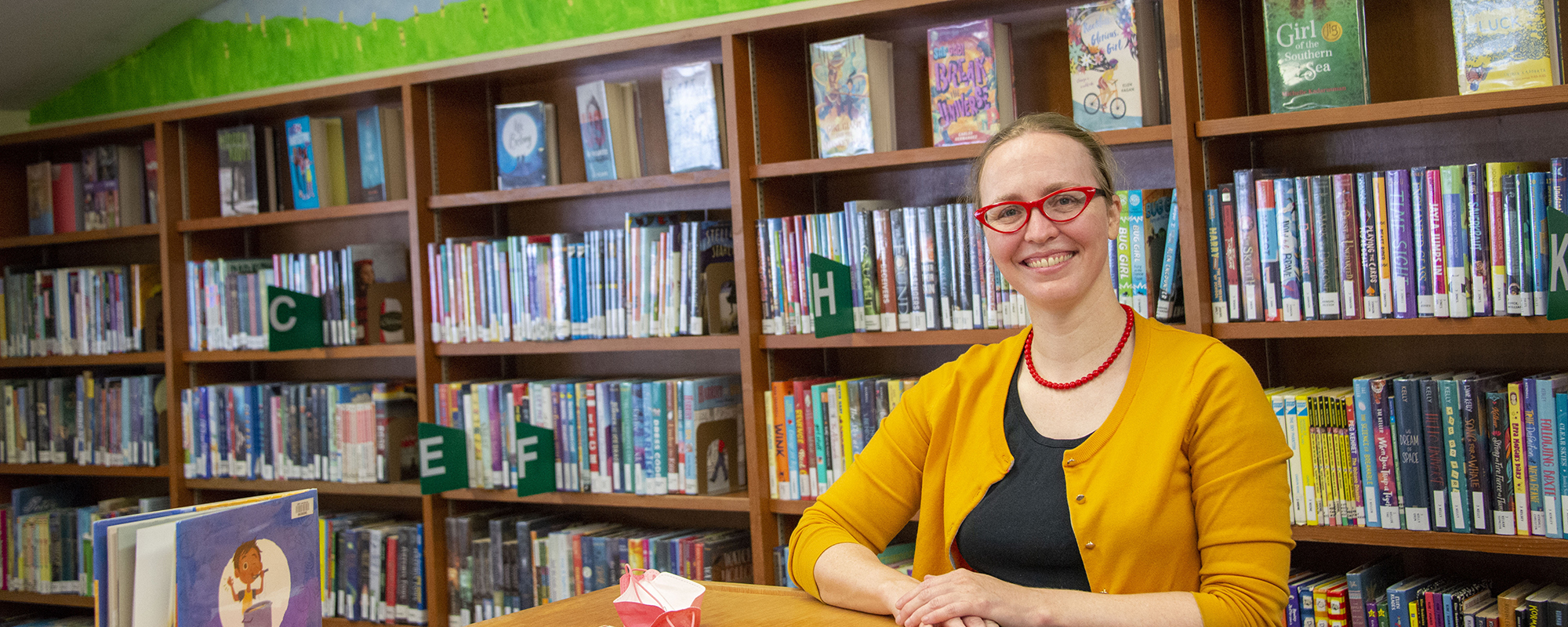 Childrens librarian smiles in front of wall of books