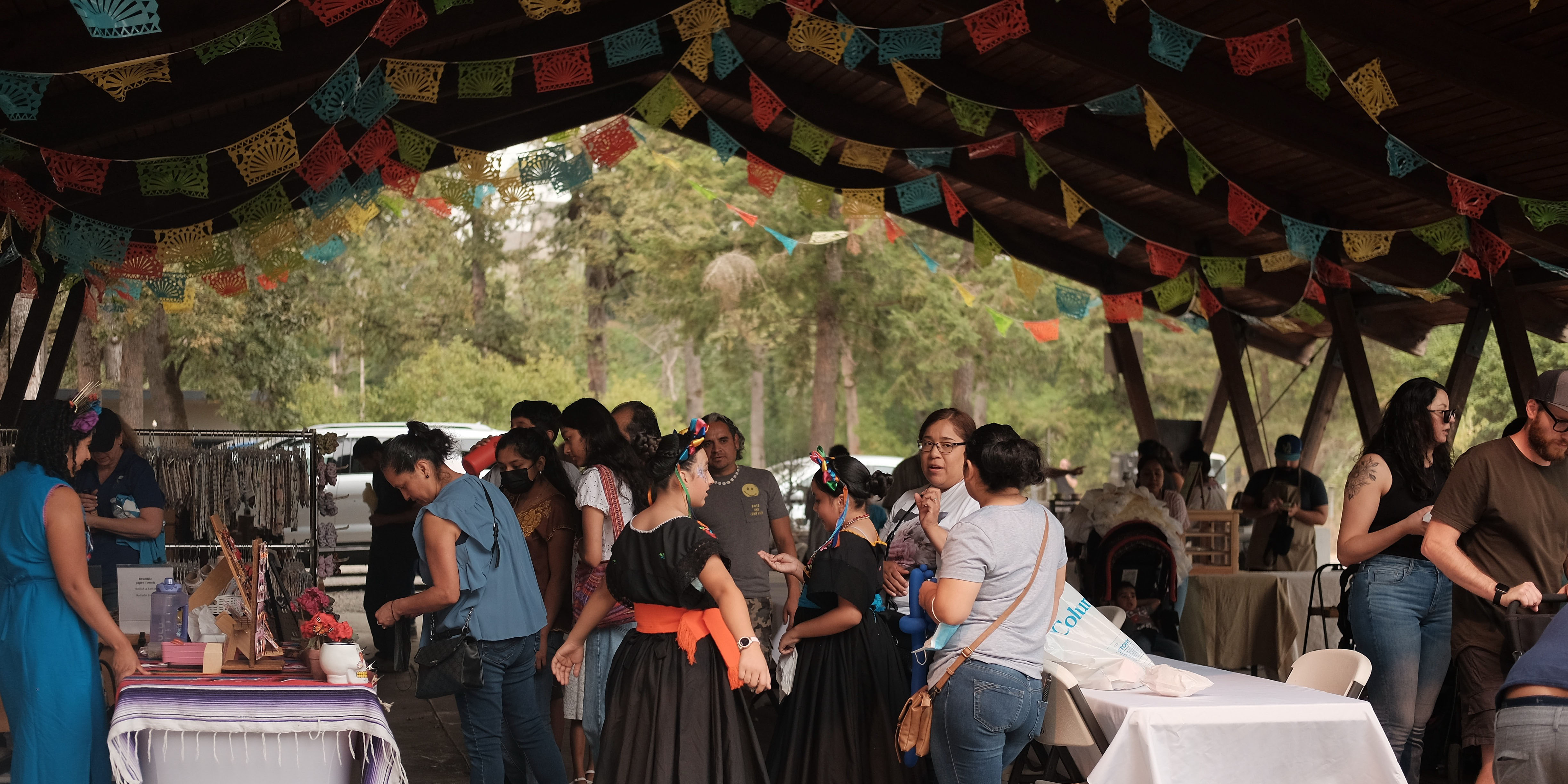 A crowd of people enjoy food under a picnic shelter