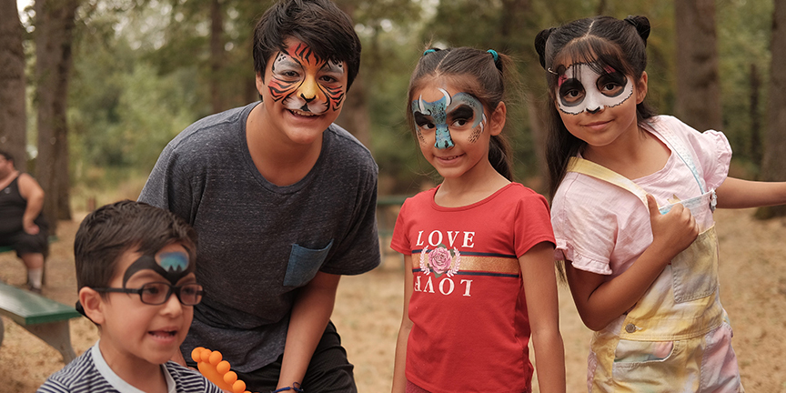 Four kids in animal face paint smile at the camera
