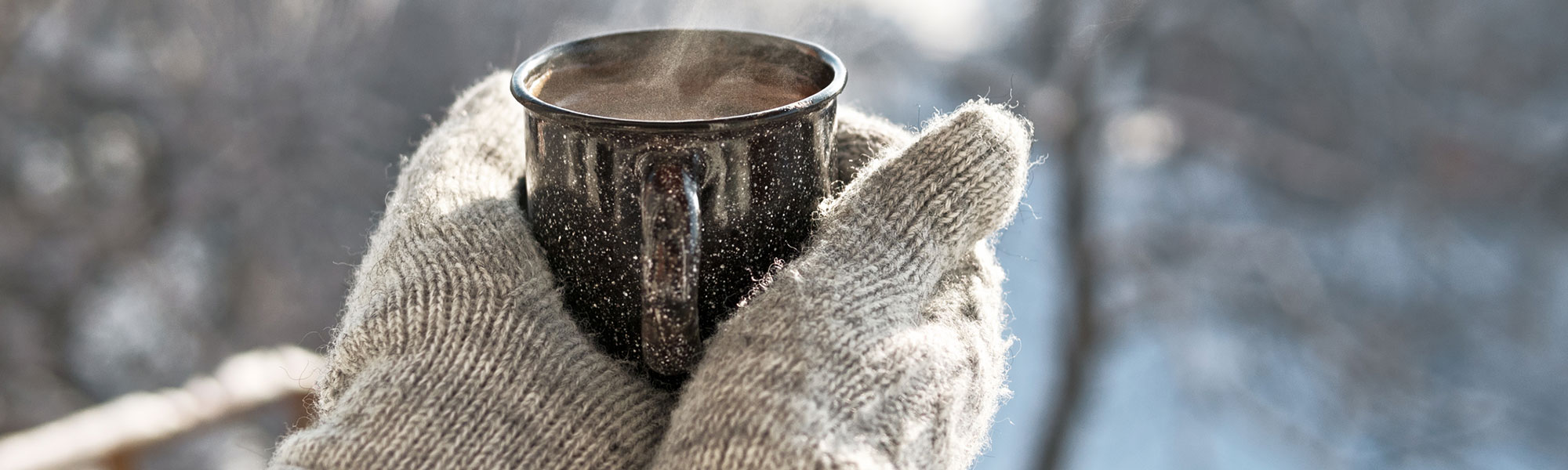 Person wearing mittens holding a warm beverage outside while snowing