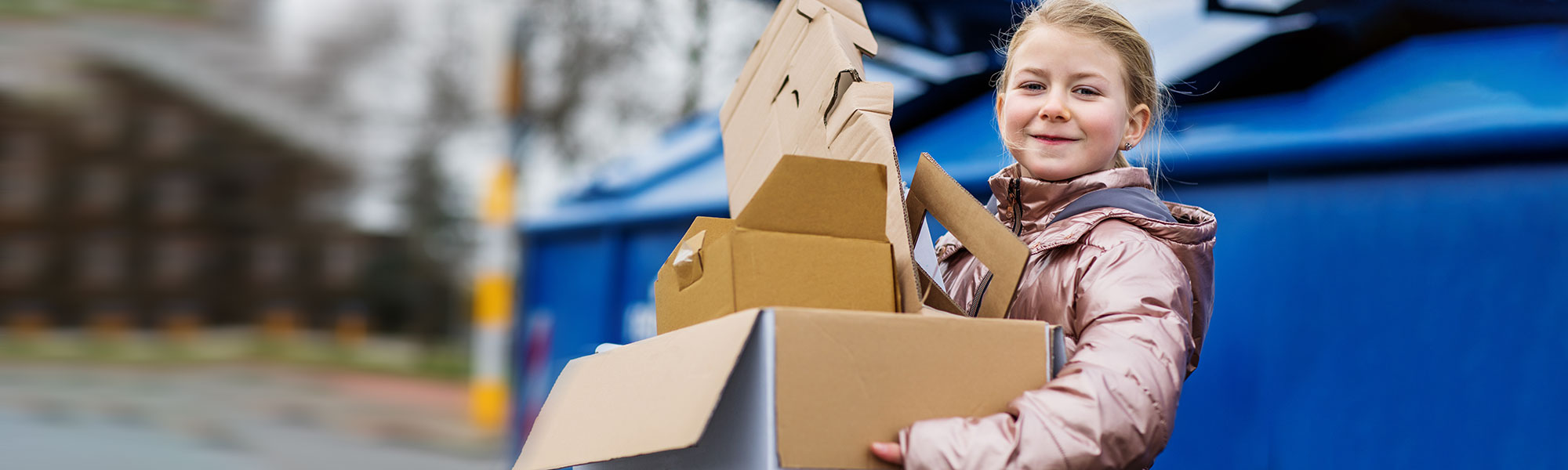 Little girl holding a box of recyclables outside her family's apartment building