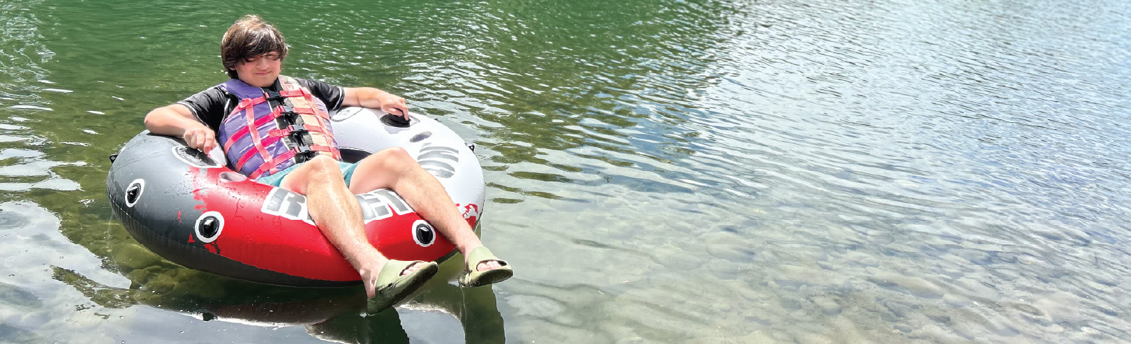 Person in life jacket sitting in inner tube on river floating