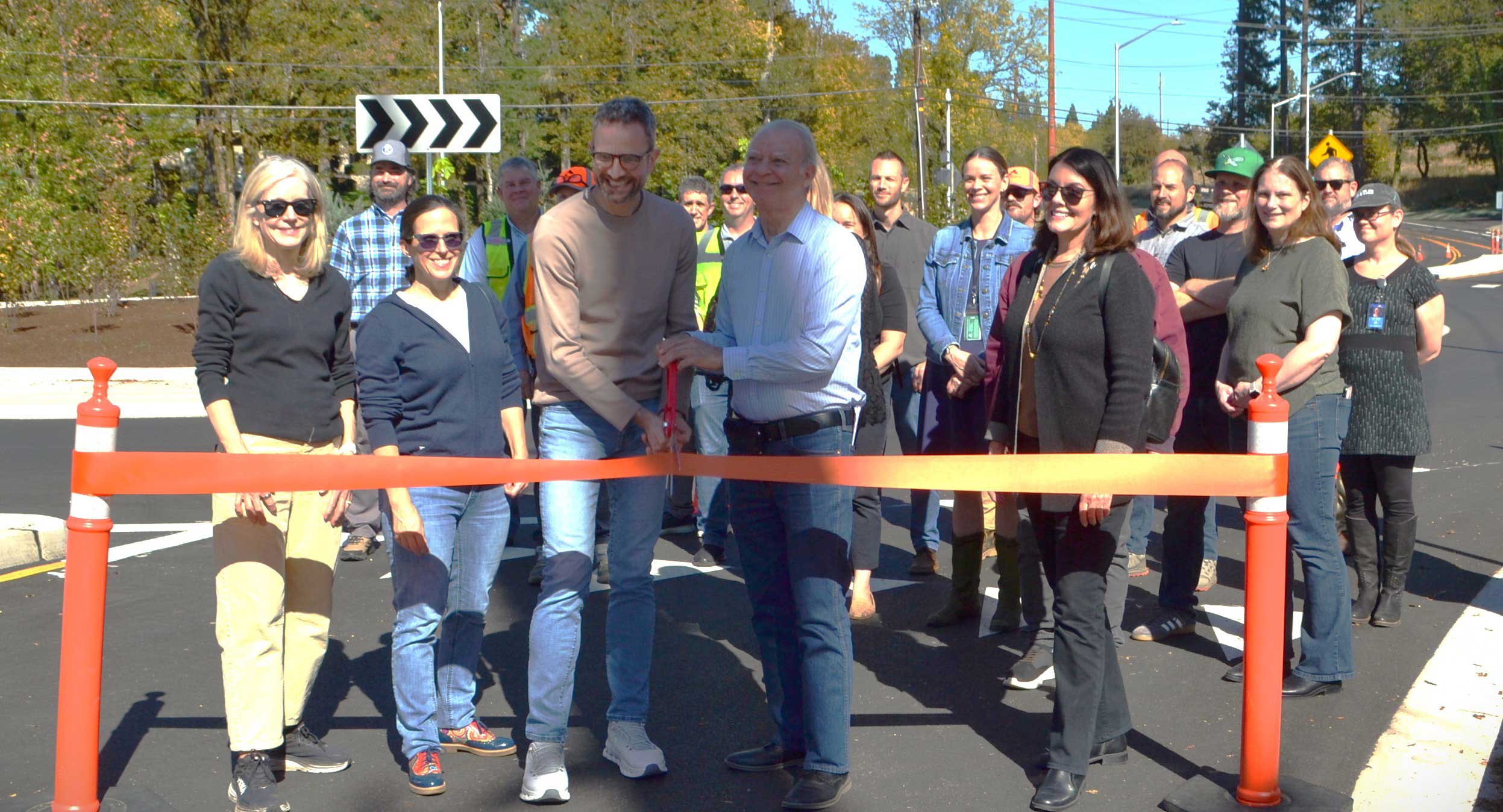 Lake Oswego Mayor Joe Buck and Clackamas County Commissioner Paul Savas cut the ribbon with a pair of ceremonial scissors at the opening of the Stafford Roundabout on Sept. 30, 2026. Also present at the ribbon are Lake Oswego Councilors Trudy Corrigan and Rachel Verdick, and Clackamas County Commissioner Diana Helm. Many people stand behind them.