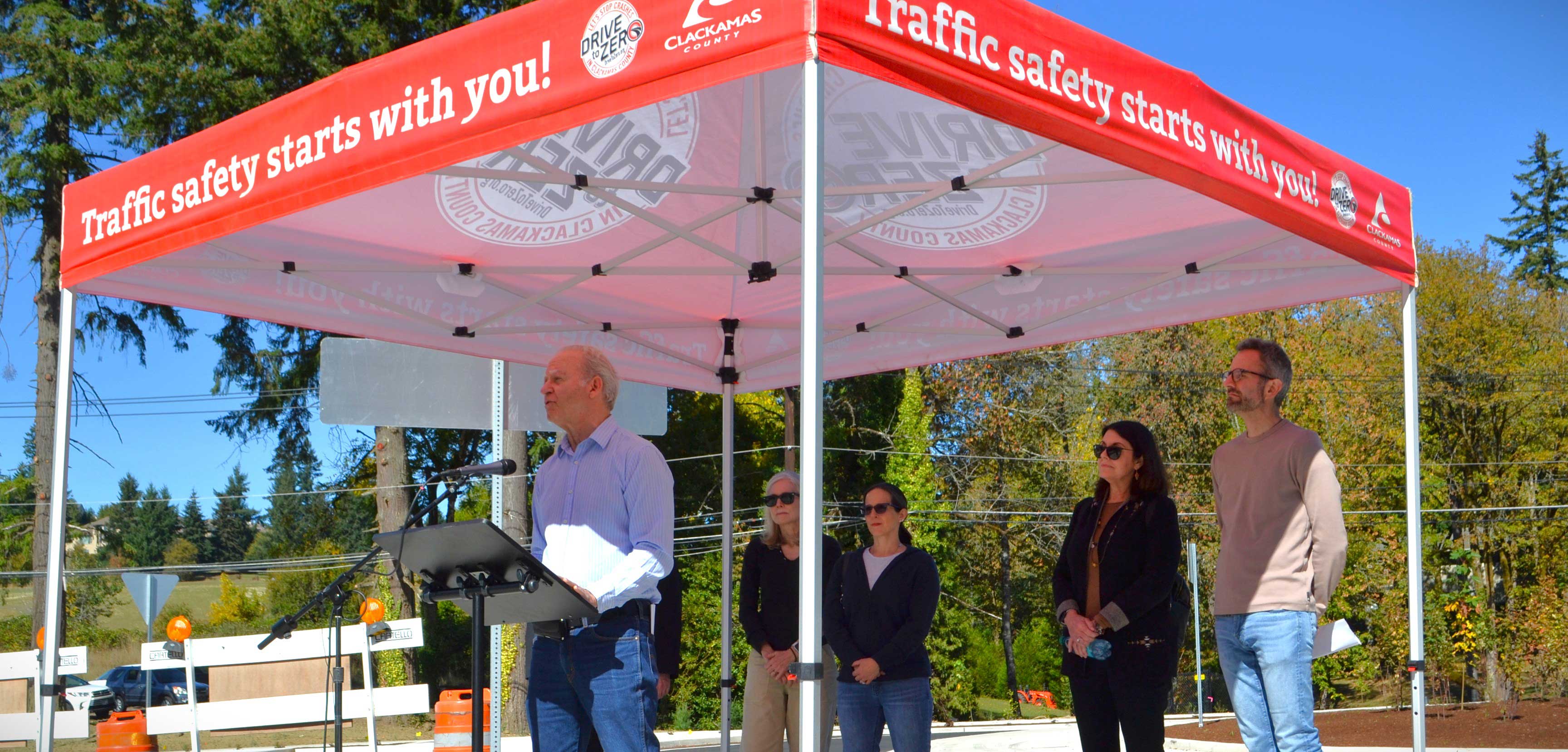 Clackamas County Commissioner Paul Savas speaks at the opening of the Stafford Roundabout on Sept. 30, 2026. Behind him are Lake Oswego Councilors Trudy Corrigan and Rachel Verdick, Clackamas County Commissioner Diana Helm, and Lake Oswego Mayor Joe Buck. Above them is a Clackamas County Drive to Zero tent, with the words Traffic safety starts with you! on it.