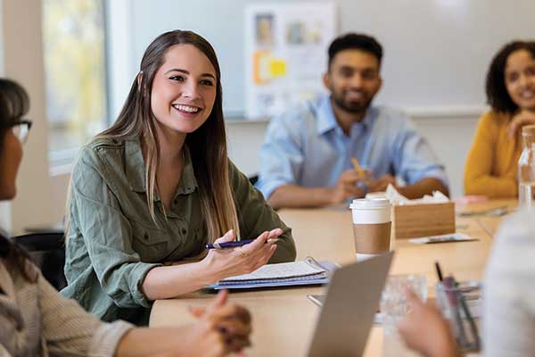 Woman at table with notebook talking with group circled around