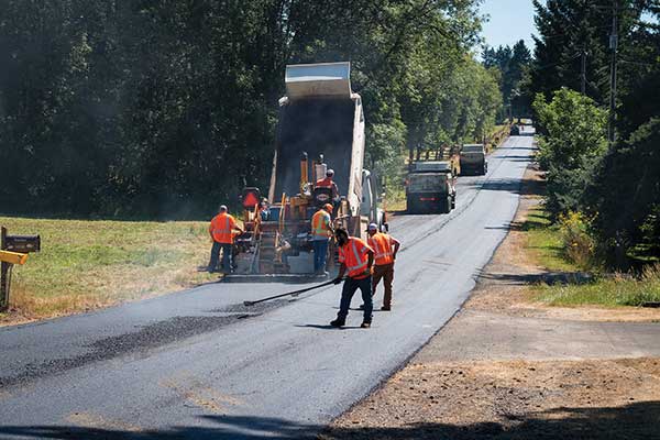 Paving crew working on road, standing behind asphalt truck