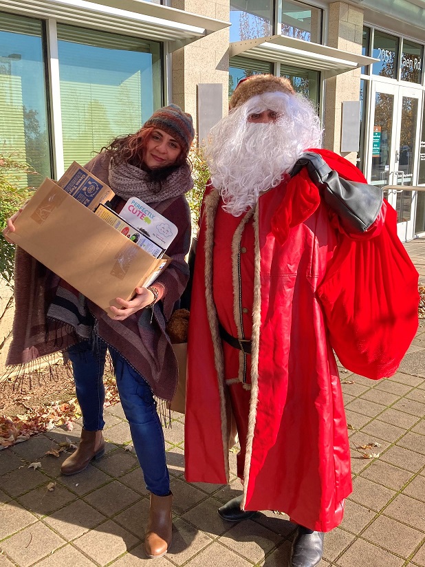 Woman holding a box of presents standing next to Santa Clause