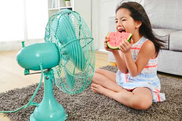 young girleating watermelon in front of a fan
