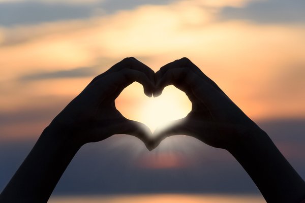 Hands making a heart shape in front of a sun rise/set