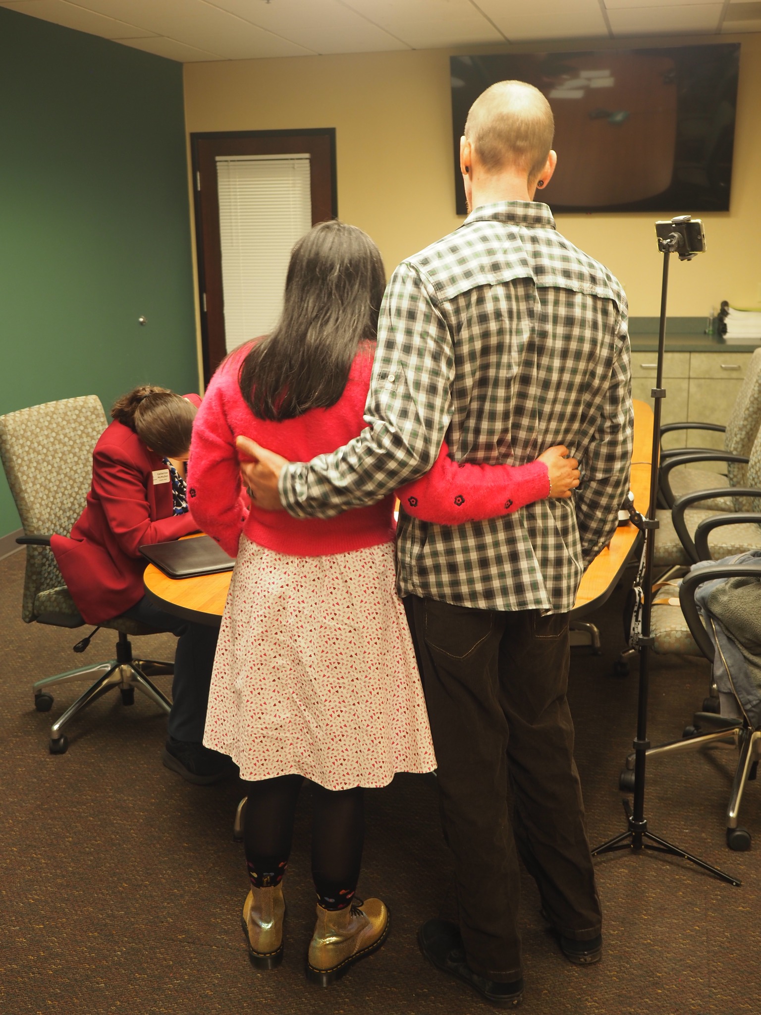 A couple stands arm in arm while the clerk completes the marriage documents