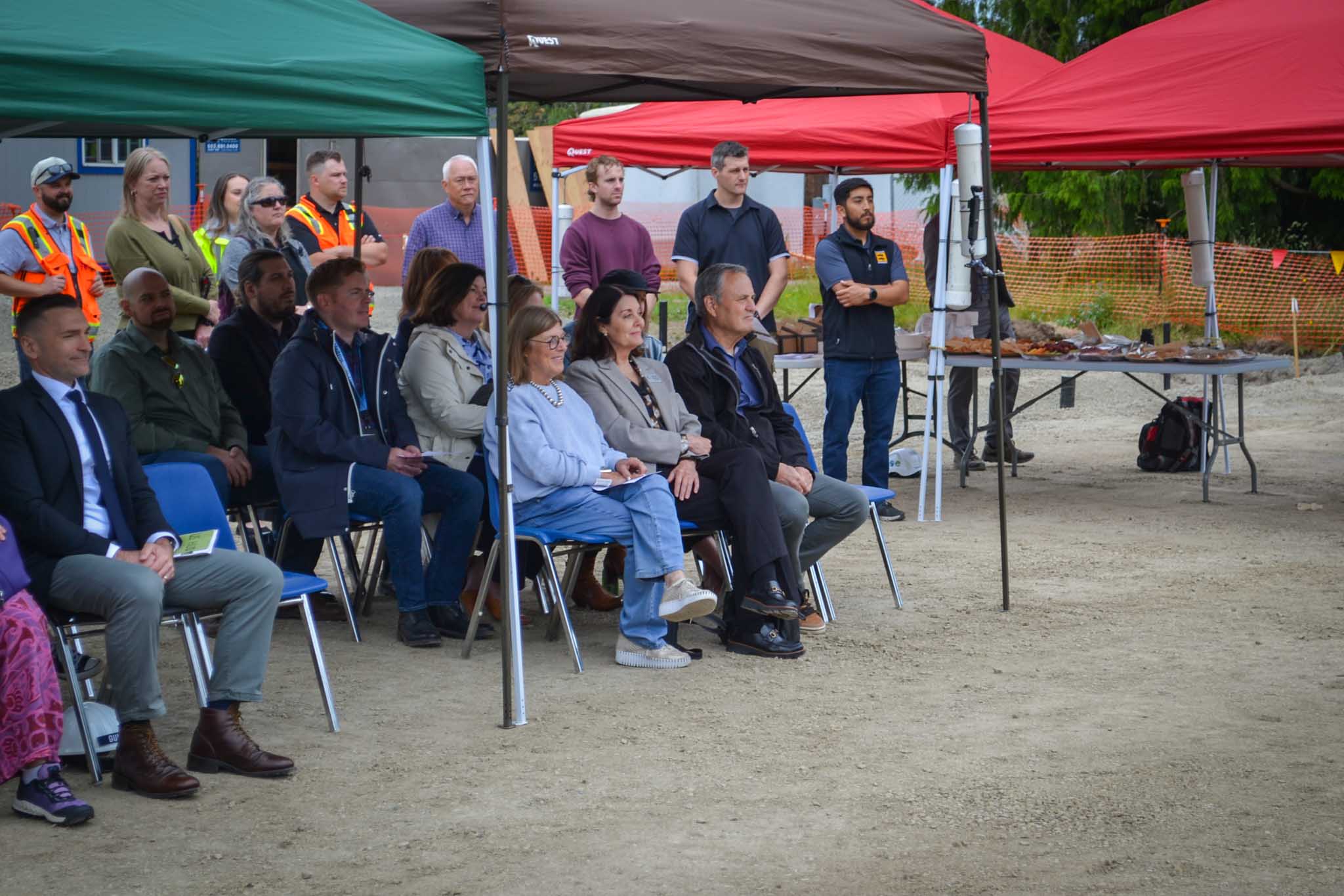 Audience of people watching groundbreaking event under shade tents