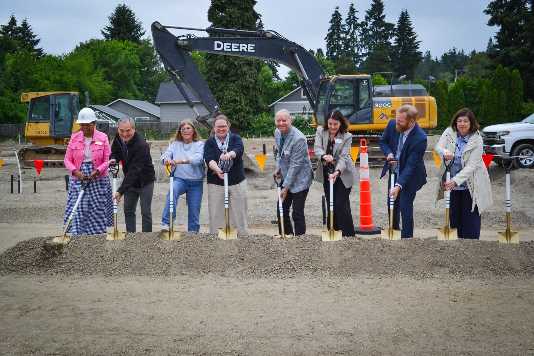 Eight people holding golden shovels in front of construction equipment at groundbreaking event 