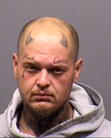 Mugshot of bald person with tattoos