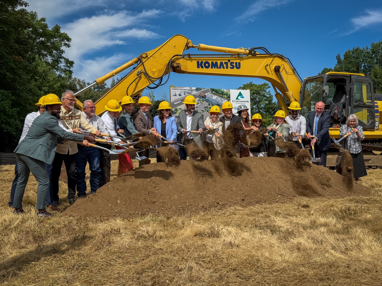 Elected officials throw dirt in the air with shovels with a piece of construction equipment behind them, at the Clackamas County Recovery Campus groundbreaking on July 29, 2026. They are out in a field and all looking up toward a photographer.