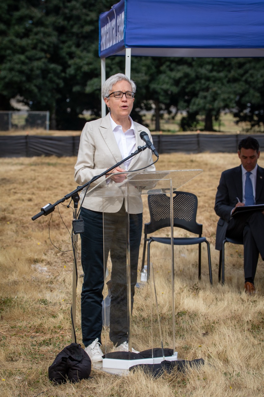 Governor Tina Kotek speaks behind a lectern at the Clackamas County Recovery Campus groundbreaking on July 29, 2026. Oregon Senate President Rob Wagner is seated in the background.