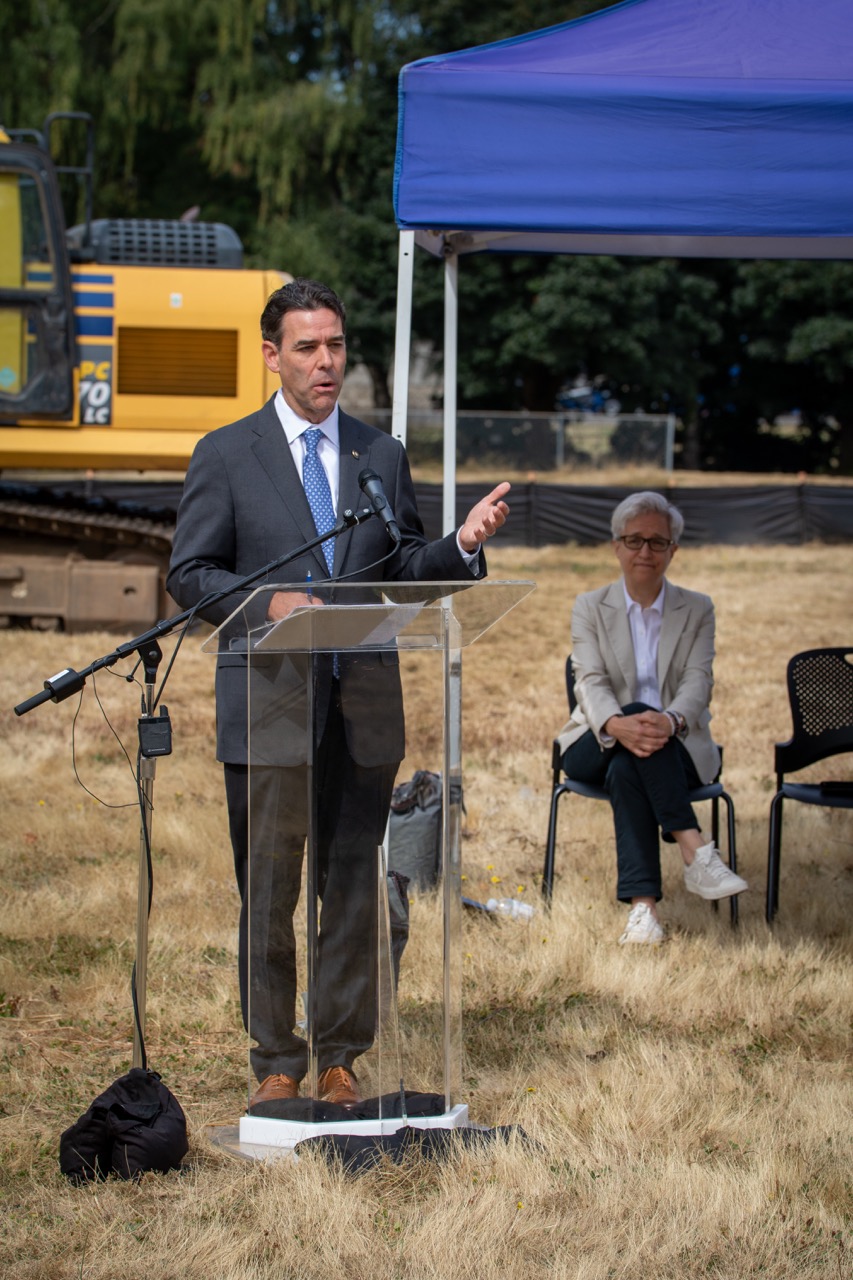 Oregon Senate President Rob Wagner speaks behind a lectern at the Clackamas County Recovery Campus groundbreaking on July 29, 2026. Governor Tina Kotek is seated in the background.