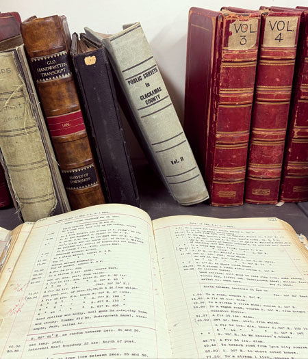 Old recordkeeping books in the background with an opened recordkeeping book in the foreground.