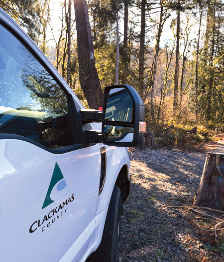 White truck, with the Clackamas County logo on the passenger side door, parked near trees.