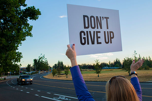 Woman holding up a sign that says "Don't give up" at a sign rally