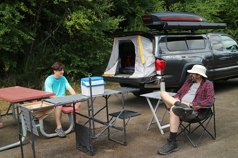 Two men having a conversation while sitting next to a camper van