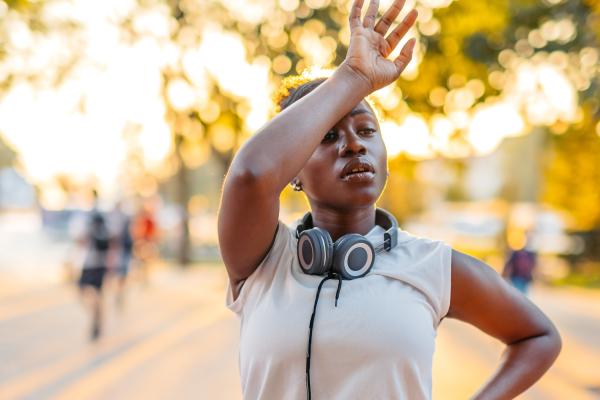 Woman wiping sweat from her forehead after a jog on a hot day
