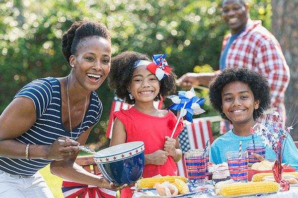 A family sitting together at a picnic table for a Fourth of July barbecue in their backyard