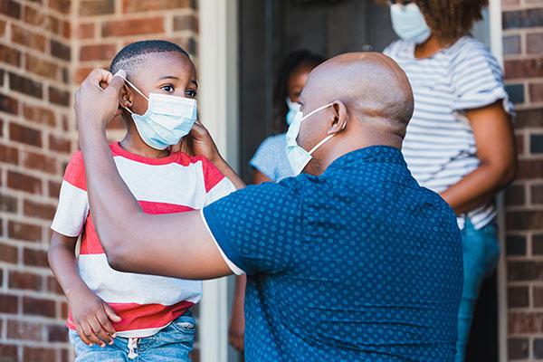 A father helps his young son put on a protective face mask before leaving their home amid the coronavirus pandemic.