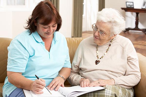 Woman helping an older adult senior woman with paper work, reading, writing while sitting on a couch