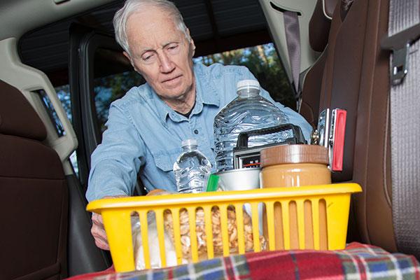 LV Senior man prepares for roadside emergency with survival items in his truck. As severe winter weather hits, this man loads a basket of survival items and a warm blanket into the back of his truck.