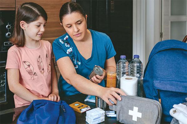 Mother preparing emergency backpack with her daughter in the kitchen