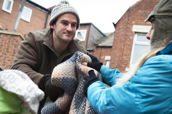 Homeless woman sitting on the street in the cold. A kind male offers her a blanket.