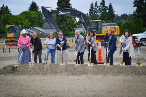 People standing in a line with golden shovels placed in dirt as though they are digging