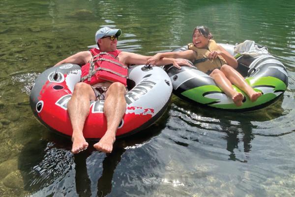 Two people in life jackets floating on inner tubes in river