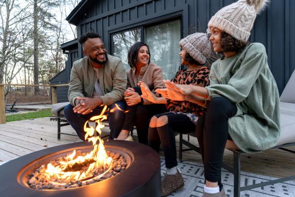 Family of 4 sitting around a fire on the porch of a cabin