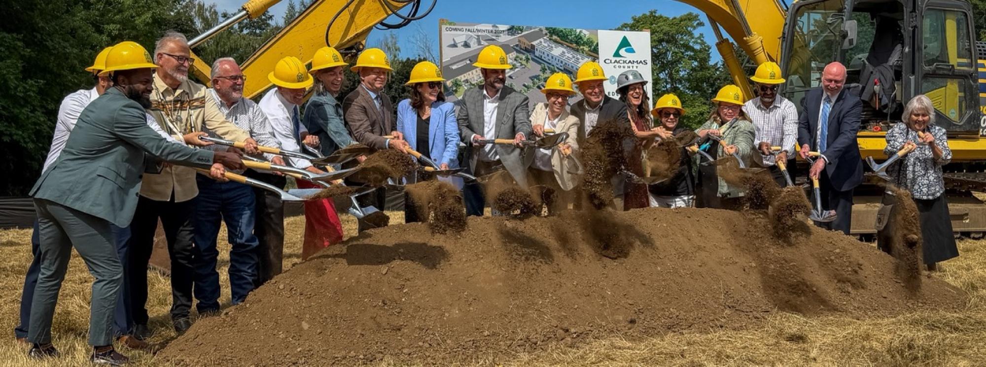 A large group of people with shovels lifting dirt into the air in front of a tractor