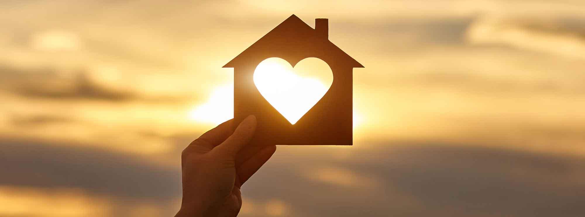 Hand holding a paper cutout of a house with heart